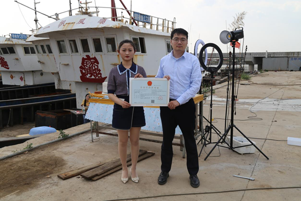 海鮮電商張夢(mèng)琴與幫辦員手持食品經(jīng)營(yíng)許可證合影。贛榆區(qū)委宣傳部供圖