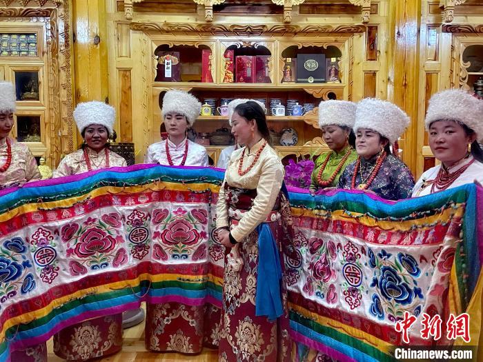 圖為女性展示村民自發(fā)繡制的“百米五彩哈達(dá)”。　李玉峰 攝