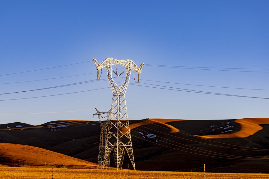 阿里地區(qū)的曠野上，電力鐵塔在夕陽下熠熠生輝。